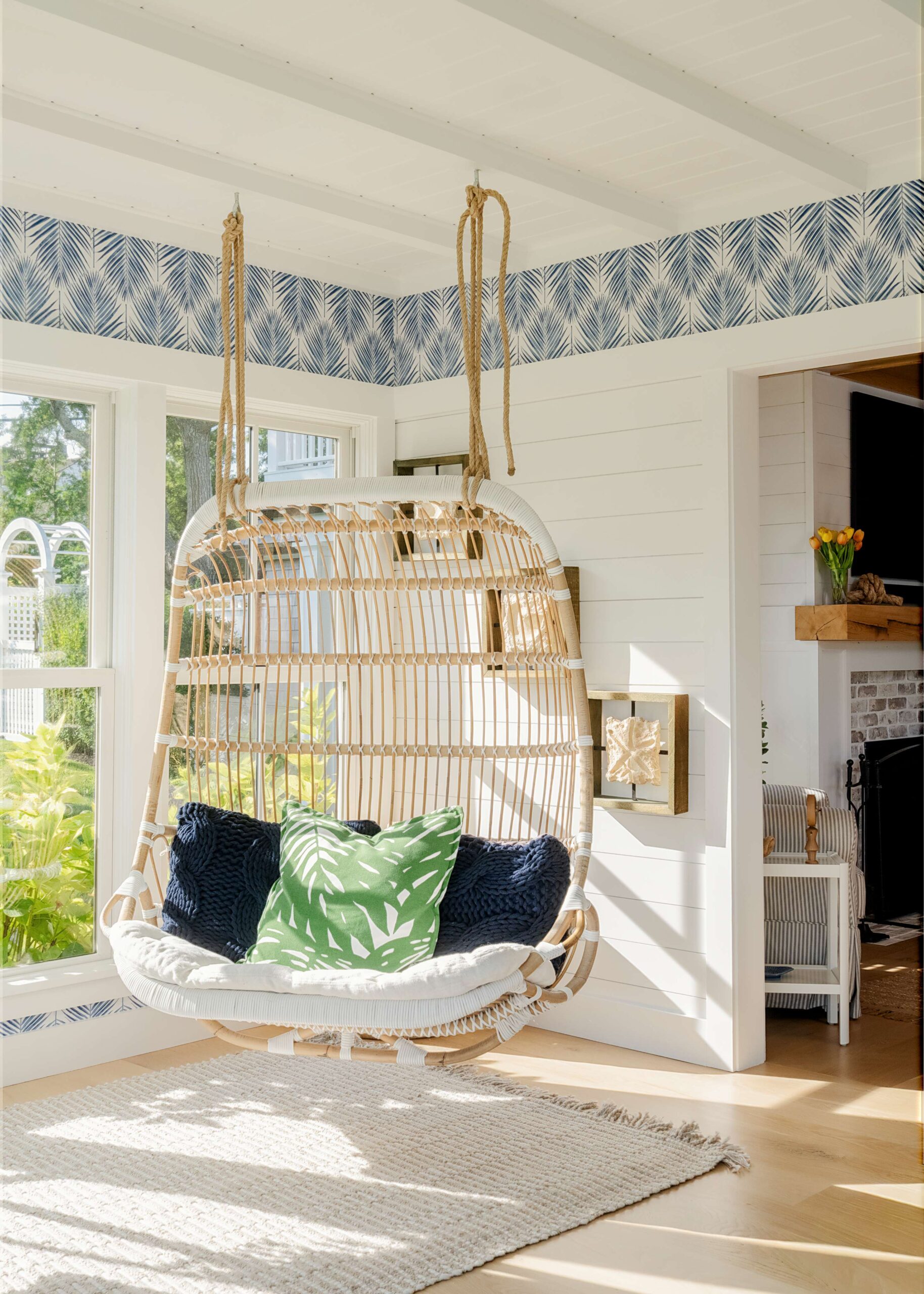 A coastal sunroom with a rattan chair and blue printed wallpaper