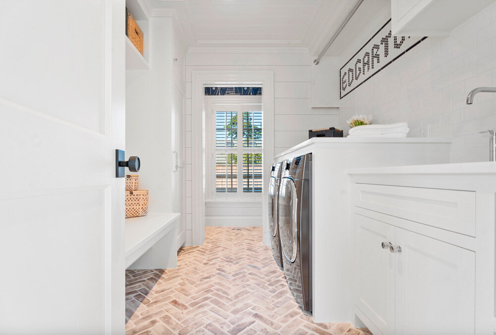 A coastal-inspired laundry room with white shiplap walls and brick flooring 