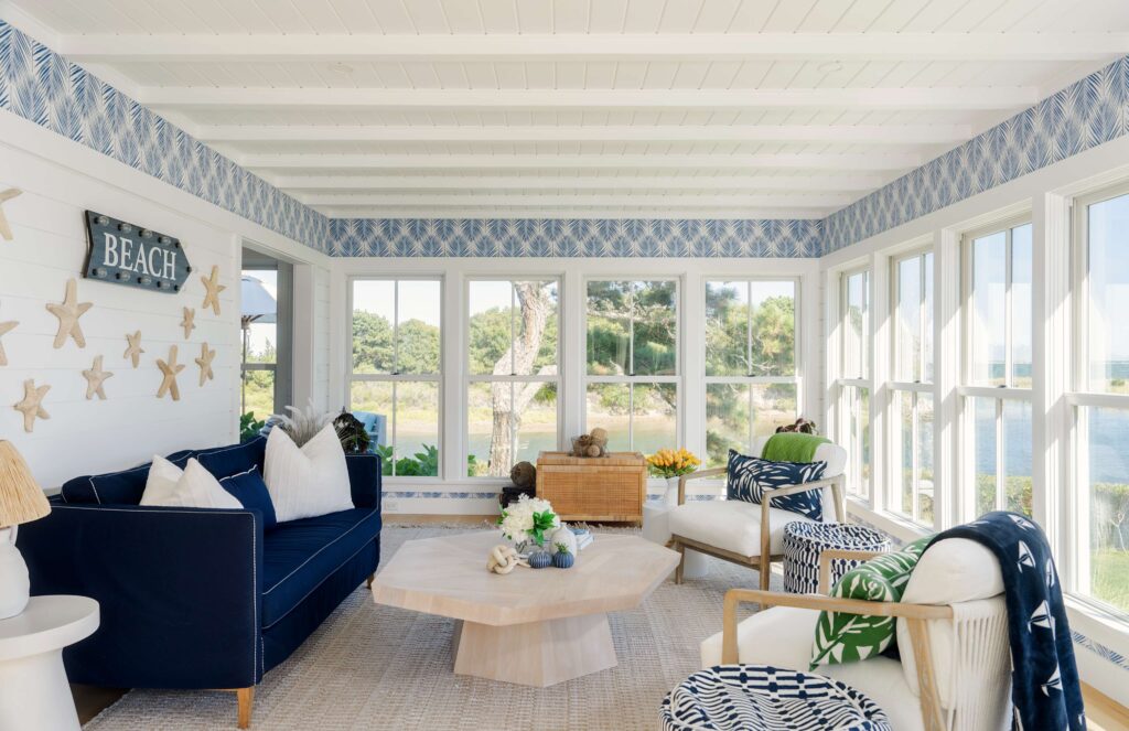A coastal sun room featuring a navy blue sofa, coastal wallpaper, and natural materials  